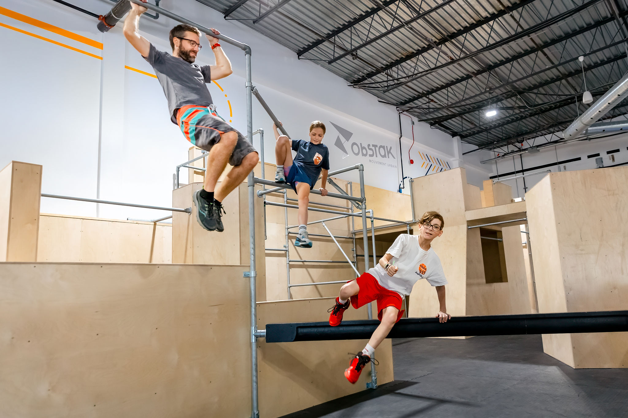 Des jeunes et des adultes en famille franchissent des obstacles de Parkour dans l&rsquo;aire d&rsquo;entra&icirc;nement d&rsquo;Obstak.